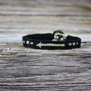 Puede incluir: Pulsera de amistad negra con un diseño de flecha verde. La pulsera está hecha con un patrón tejido y tiene un cierre de metal.