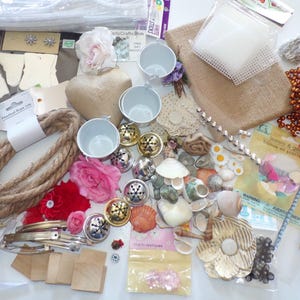 May include: A collection of craft supplies including twine, seashells, bells, fabric flowers, beads, and small metal containers.
