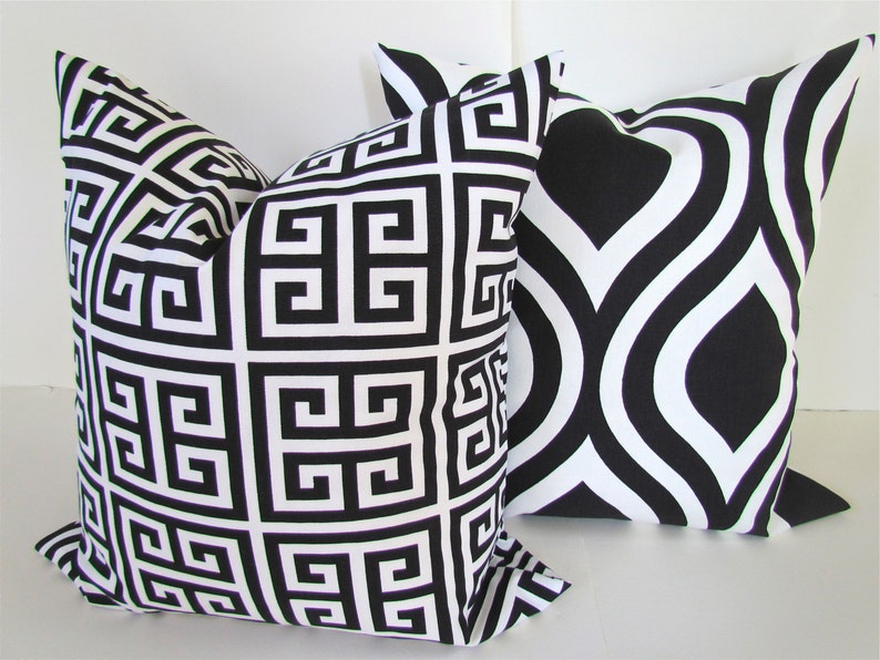 May include: Two decorative throw pillows with black and white geometric patterns. One pillow features a Greek key design, while the other has a swirling, abstract pattern.