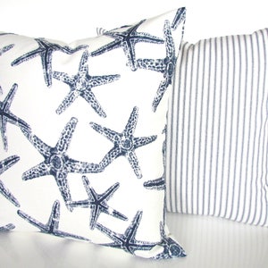 May include: Two decorative throw pillows, one with a white background and a navy blue starfish pattern, and the other with a white background and thin navy blue stripes.