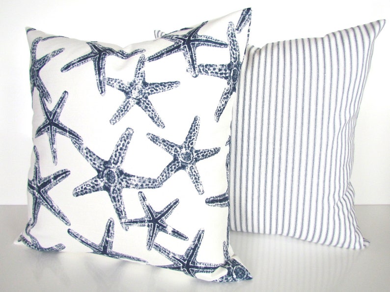 May include: Two decorative throw pillows, one with a white background and a navy blue starfish pattern, and the other with a white background and thin navy blue stripes.