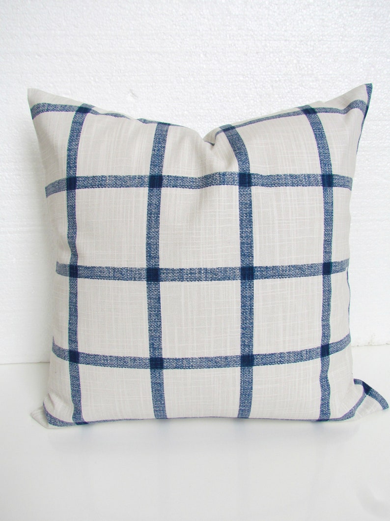 May include: A white pillow with a navy blue plaid pattern. The pillow is made of a soft, textured fabric.