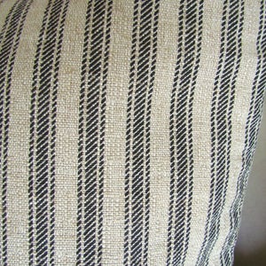 May include: Close-up of a beige and black striped fabric. The fabric has a woven texture and is made of natural fibers.