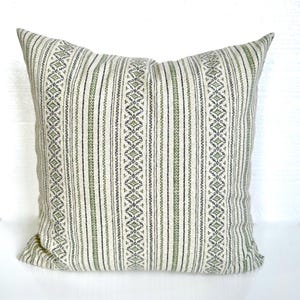 May include: A white pillow with green and black stripes and a geometric pattern. The pillow is made of a soft, woven fabric.