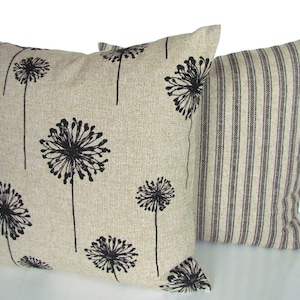 May include: Two decorative throw pillows. One pillow is beige with a black dandelion print. The other pillow is beige with black vertical stripes.