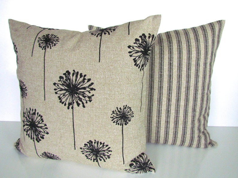 May include: Two decorative throw pillows. One pillow is beige with a black dandelion print. The other pillow is beige with black vertical stripes.