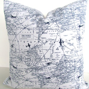 Può includere: Un cuscino bianco con una stampa di mappa del mondo blu navy. La mappa presenta icone di aerei e il testo "Il Mondo" in stile vintage.