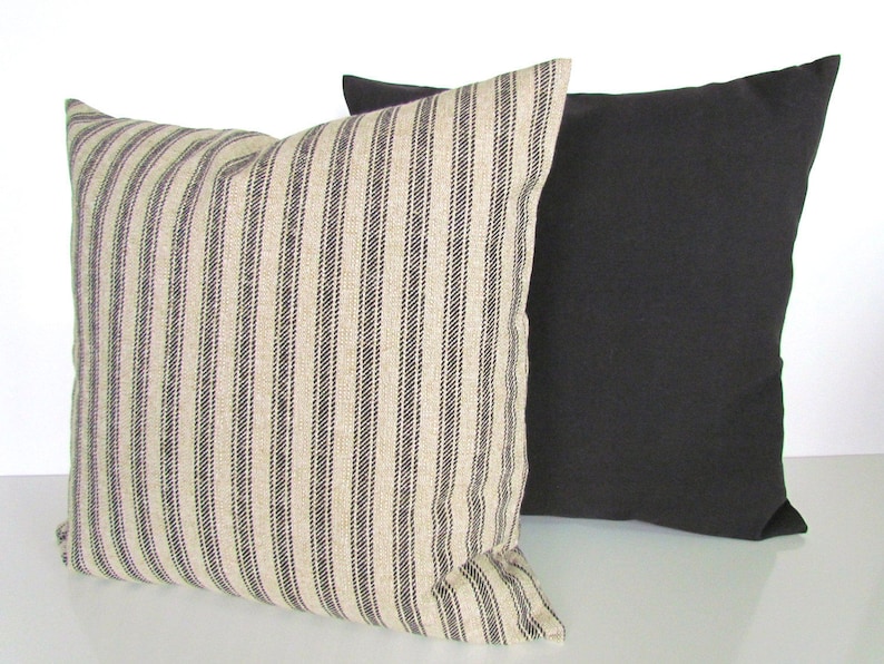 May include: Two decorative throw pillows, one with black and white stripes and one solid black. The striped pillow is made of a textured fabric.