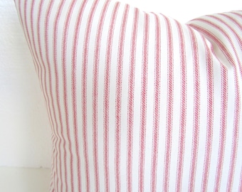 May include: Close-up of a white pillow with vertical red stripes. The pillow has a soft, textured appearance, with the stripes evenly spaced across the fabric. The pillow is a decorative item.