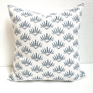 May include: White cushion with a blue floral pattern. The pattern is a repeating design of stylised flowers with a dark blue centre.