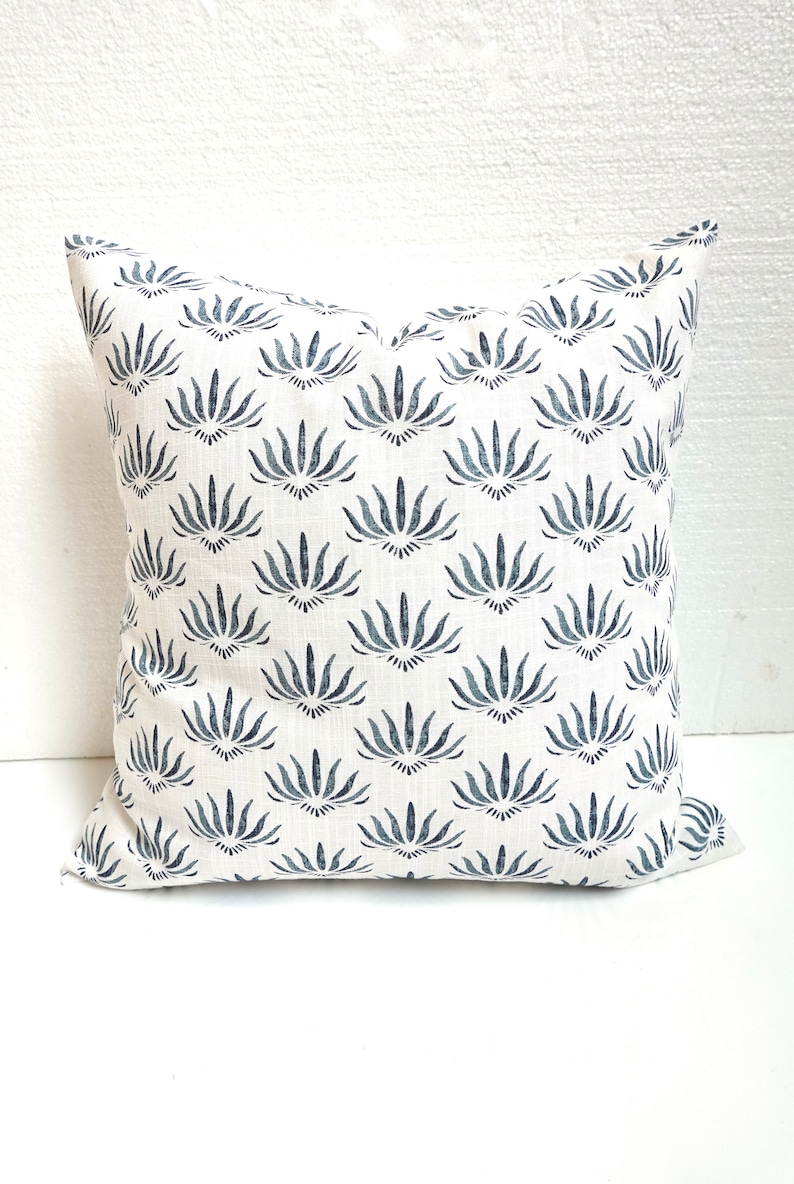 May include: White cushion with a blue floral pattern. The pattern is a repeating design of stylised flowers with a dark blue centre.