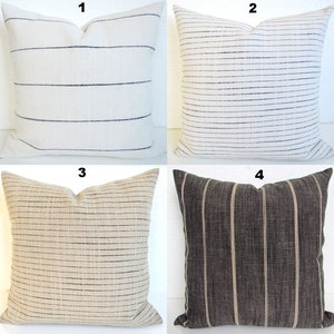 May include: Four decorative throw pillows with striped patterns. The pillows are in various colors, including white, beige, black, and gray. The stripes are thin and create a subtle, elegant design.