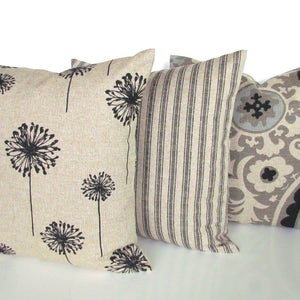 May include: Three decorative throw pillows with a neutral color scheme. One pillow features a black and white dandelion print, another has black and white stripes, and the third has a black, gray, and white paisley pattern.