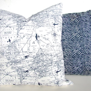 May include: Two decorative throw pillows. One pillow features a vintage world map with airplane illustrations and the text "The World". The other pillow has a navy blue and white chevron pattern.