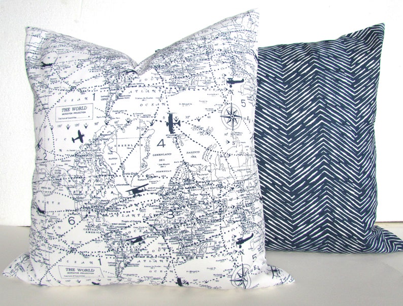 May include: Two decorative throw pillows. One pillow features a vintage world map with airplane illustrations and the text "The World". The other pillow has a navy blue and white chevron pattern.