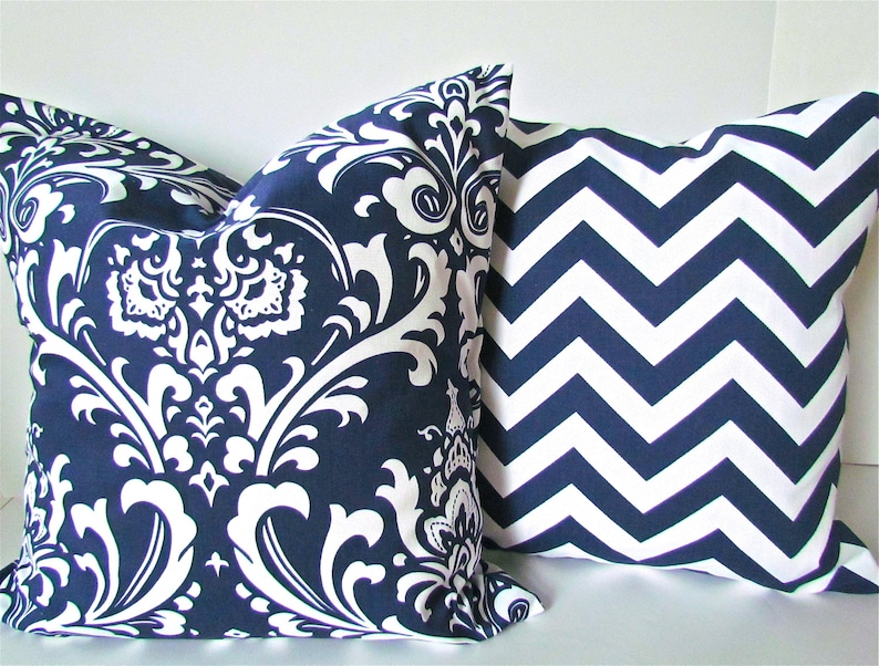 May include: Two decorative throw pillows, one with a navy blue and white damask pattern and the other with a navy blue and white chevron pattern.