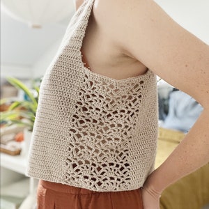May include: A beige crochet tank top with a lacy design on the sides. The top is sleeveless and cropped.