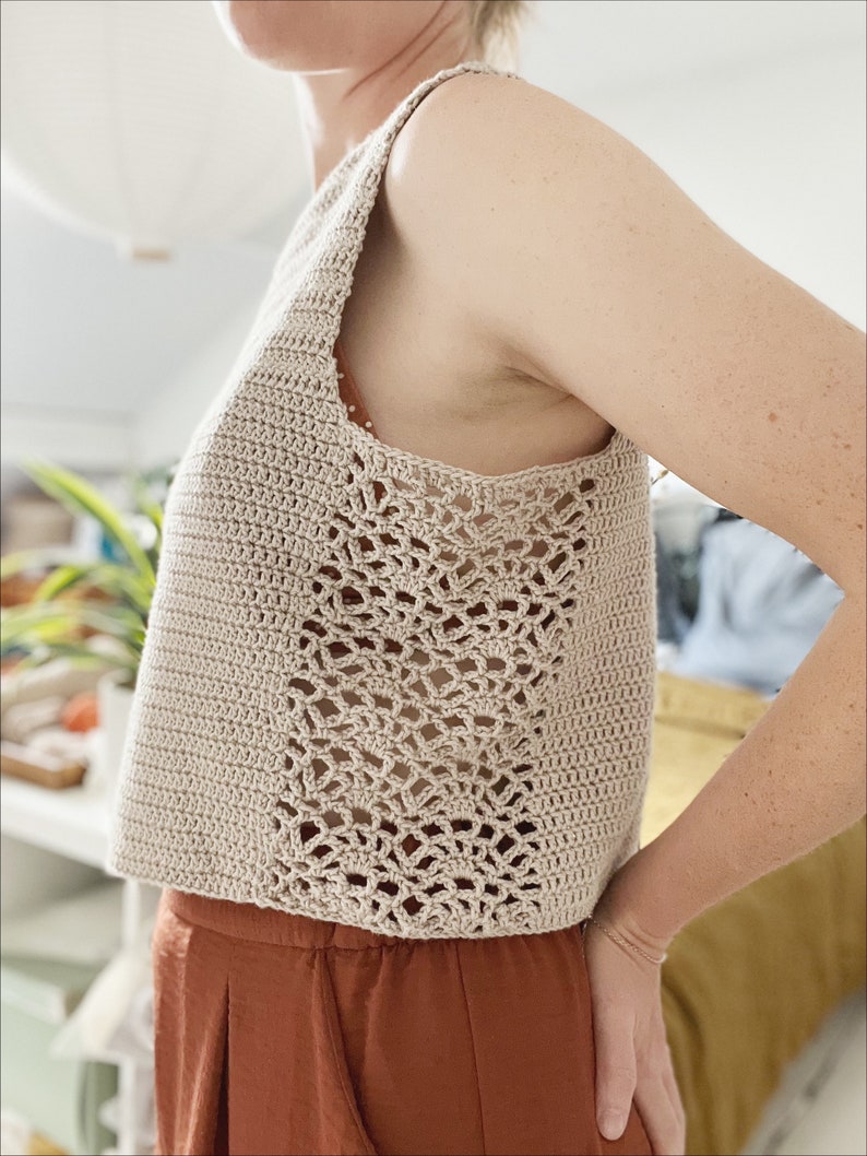May include: A beige crochet tank top with a lacy design on the sides. The top is sleeveless and cropped.