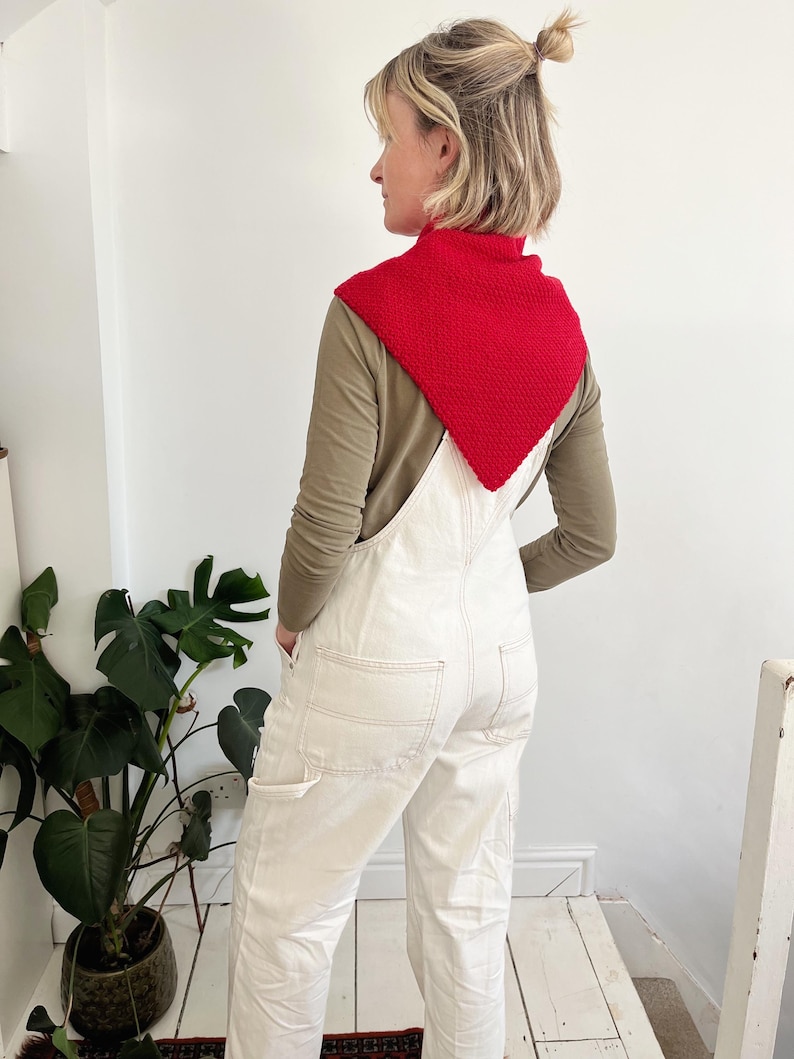 Peut inclure: Un col tricot&eacute; rouge port&eacute; sur un haut &agrave; manches longues vert olive et une salopette blanche. Le col est de forme carr&eacute;e et textur&eacute;e. La salopette a des poches et des d&eacute;tails de couture. La tenue est d&eacute;contract&eacute;e et &eacute;l&eacute;gante.