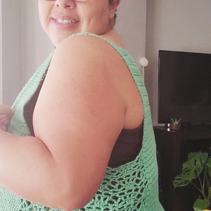 May include: A woman wearing a green crochet top with a floral headband. The top has a delicate openwork pattern and is worn over a patterned skirt.
