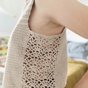 May include: A beige crochet tank top with a delicate openwork design on the sides. The top is cropped and has a relaxed fit.