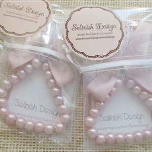 May include: Two packages of pink pearl bracelets, each in a clear bag with a pink ribbon. Each package has a tag with the text "Selinish Design" and the Etsy shop URL.