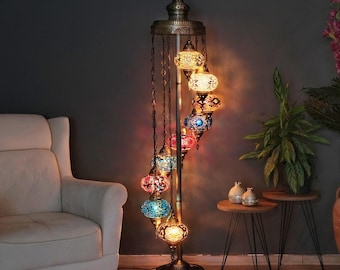 May include: A tall floor lamp with a dark metal stand and a central pole. It features nine hanging glass mosaic globes in various colors including blue, red, orange, and white, arranged in a spiral pattern. The lamp has a decorative metal top.