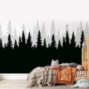 May include: A black and white silhouette of a forest with a grey background. The forest is behind a bed with a brown blanket and pillows. The bed is in a room with a wooden floor.