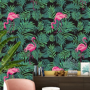May include: A black background with a repeating pattern of pink flamingos and green palm leaves. The wallpaper is displayed in a living room setting with a pink armchair, a side table, and a wooden cabinet.