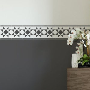 Könnte beinhalten: Ein modernes Badezimmer mit weißer Badewanne, Toilette und Bidet. Die dunkelgraue Wand hat eine dekorative Bordüre mit geometrischen schwarzen und weißen Formen. Ein Holzschrank beherbergt eine Orchidee und Badezimmerzubehör.