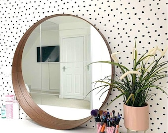 May include: A round wooden framed mirror with a white vanity table and a potted plant with white flowers. The wall behind the mirror has a black and white polka dot pattern.