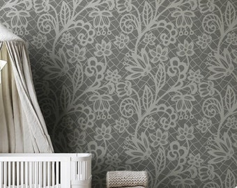 May include: A nursery scene with a white cot and canopy, set against a grey floral wallpaper. Wooden stools hold blankets and a wooden toy. A round jute rug and a white armchair complete the room's decor, creating a cozy atmosphere.