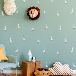 May include: A light blue nursery with a white and brown cloud-shaped pillow, a light blue armchair with a yellow star-shaped pillow, a wooden table with a white ceramic cup and a brown and white ceramic animal figurine, a woven basket with a brown and white pom-pom trim, and a light green wall with a repeating pattern of white geese.