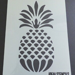 May include: A white stencil of a pineapple with a detailed design. The stencil is made for crafting and decorating projects. The stencil is labeled "IDEAL STENCILS".