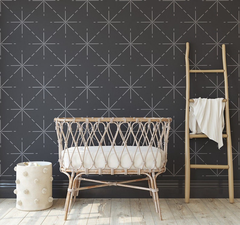 May include: A nursery scene featuring a woven rattan bassinet with a white mattress, a wooden ladder with a folded blanket, and a round, textured storage basket. The dark gray wall has a repeating white starburst pattern. The floor is light wood.