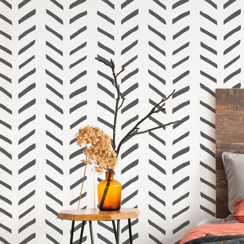 May include: A white wall with a black chevron pattern wallpaper. A wooden side table with a vase of dried flowers and a clear glass vase.