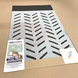 May include: A white reusable stencil with a black chevron pattern. The stencil is on a brown surface. The text "IDEALSTENCILS" is visible in the lower left corner of the image.