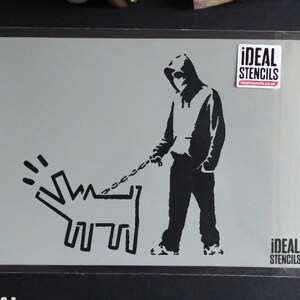May include: Black and white stencil of a person in a hooded sweatshirt walking a dog on a leash. The stencil is on a gray background and has the text "IDEAL STENCILS" on the bottom right corner.