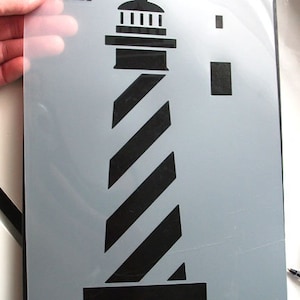 May include: A black and white lighthouse stencil with a striped design. The stencil is on a gray background and has the text "IDEAL STENCILS" in the top left corner.