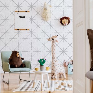 May include: A child's room with a light blue armchair, a brown teddy bear, and a tall stuffed giraffe. A small white table holds a cactus and yellow cups. The wall features a geometric pattern and animal head decorations.