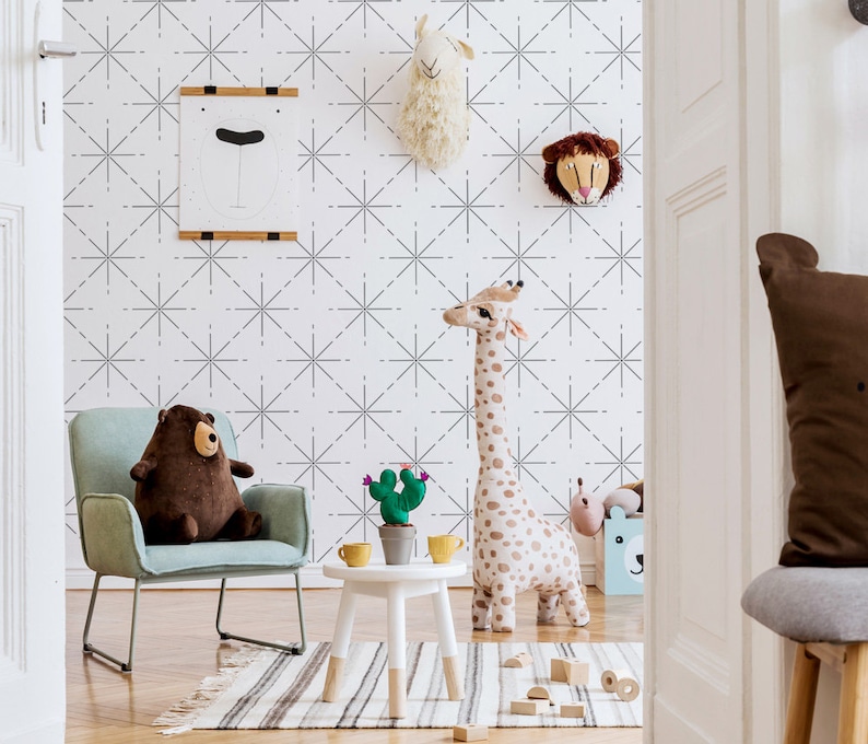 May include: A child's room with a light blue armchair, a brown teddy bear, and a tall stuffed giraffe. A small white table holds a cactus and yellow cups. The wall features a geometric pattern and animal head decorations.