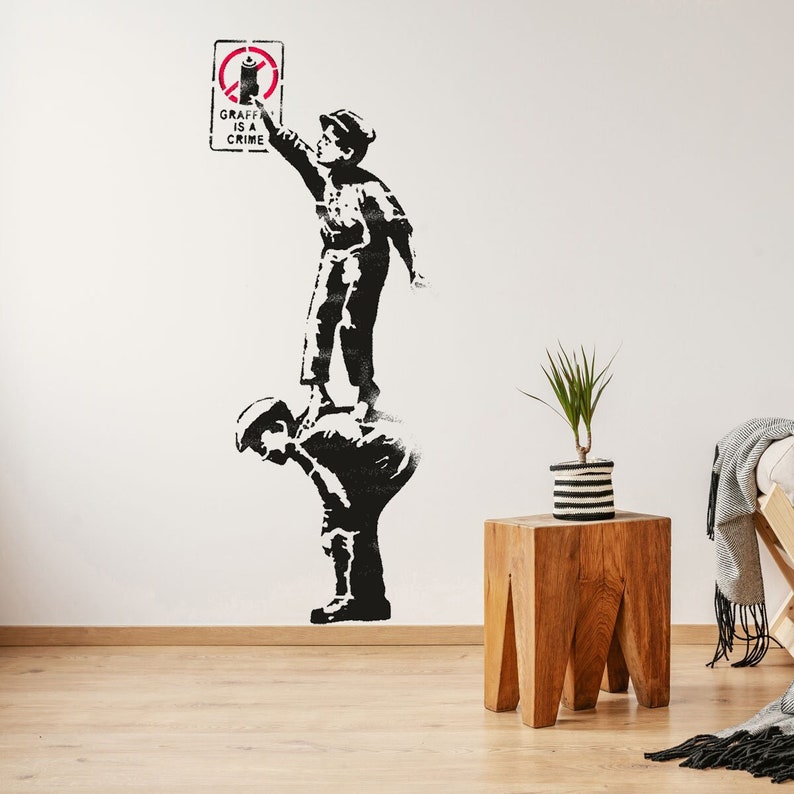 Puede incluir: Arte de est&eacute;ncil en blanco y negro de dos ni&ntilde;os en una pared blanca. El ni&ntilde;o de arriba sostiene una lata de aerosol y un cartel que dice "Graffiti is a crime".