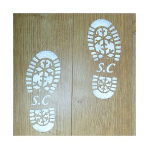 May include: Two silver boot prints on a wooden floor. The prints have a snowflake design and the initials "S.C." in the centre.