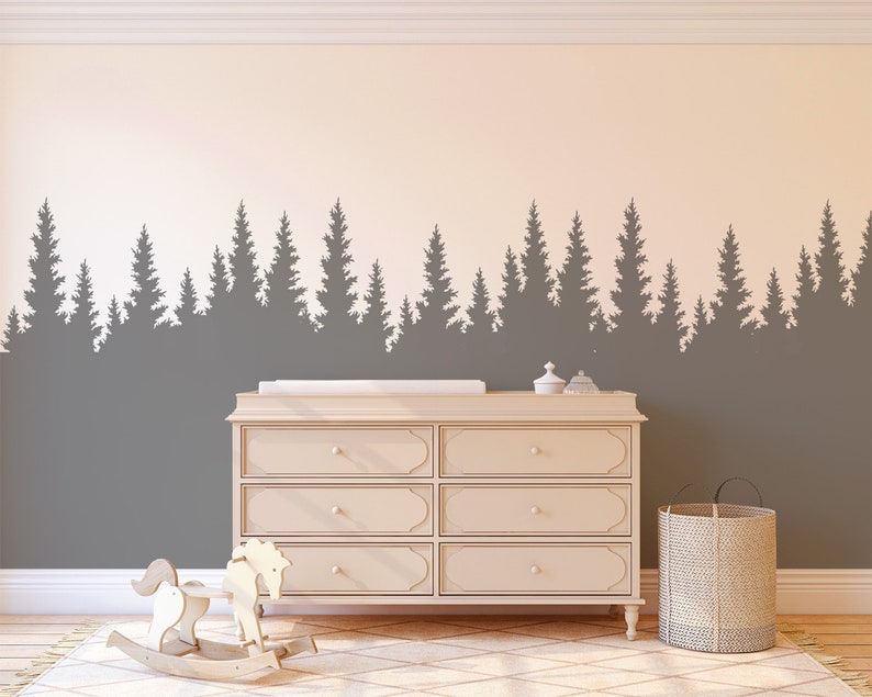 May include: A nursery room with a gray and white wall featuring a silhouette of a forest tree line. A white changing table with six drawers is in the center of the room. A rocking horse is on the left side of the changing table. A woven basket is on the right side of the changing table.