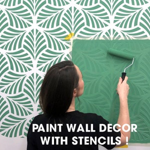 May include: A person uses a paint roller to apply green paint to a wall using a stencil. The stencil is a repeating pattern of green leaves. The text "PAINT WALL DECOR WITH STENCILS!" is at the bottom of the image.