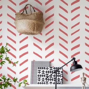 May include: A white wall with a red chevron pattern. A woven basket hangs on the wall. A black and white patterned box and a black lamp are on a white shelf.
