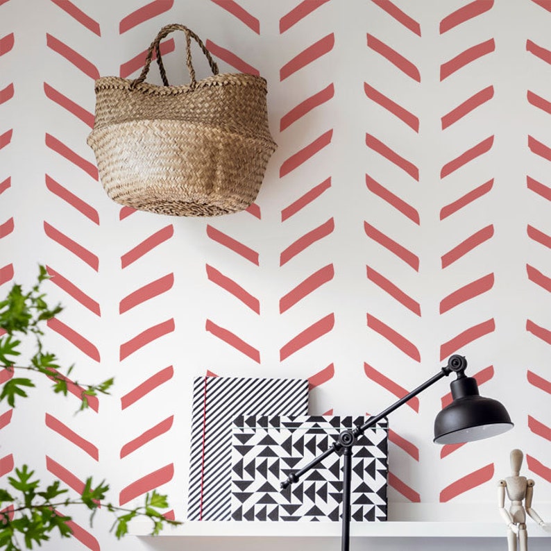 May include: A white wall with a red chevron pattern. A woven basket hangs on the wall. A black and white patterned box and a black lamp are on a white shelf.
