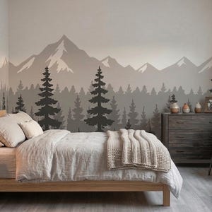 May include: A wall mural featuring a mountain range and a dense forest of pine trees in shades of gray and black. The design spans across the wall behind a wooden bed frame with light-colored bedding, a wooden nightstand, and a dark wooden dresser.