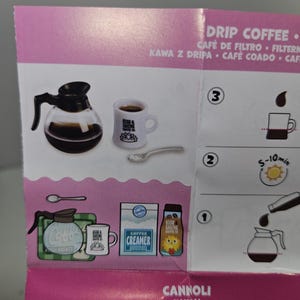 May include: A miniature coffee set with a glass carafe, a mug with the text "RISE & SHINE COFFEE CO.", and a spoon. Also shown are a coffee maker, creamer, and a bottle with a yellow label.