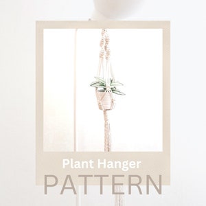 May include: A white macrame plant hanger with a small potted plant hanging from it. The hanger is made with a thick rope and has a simple design. The text "Plant Hanger PATTERN" is at the bottom of the image.